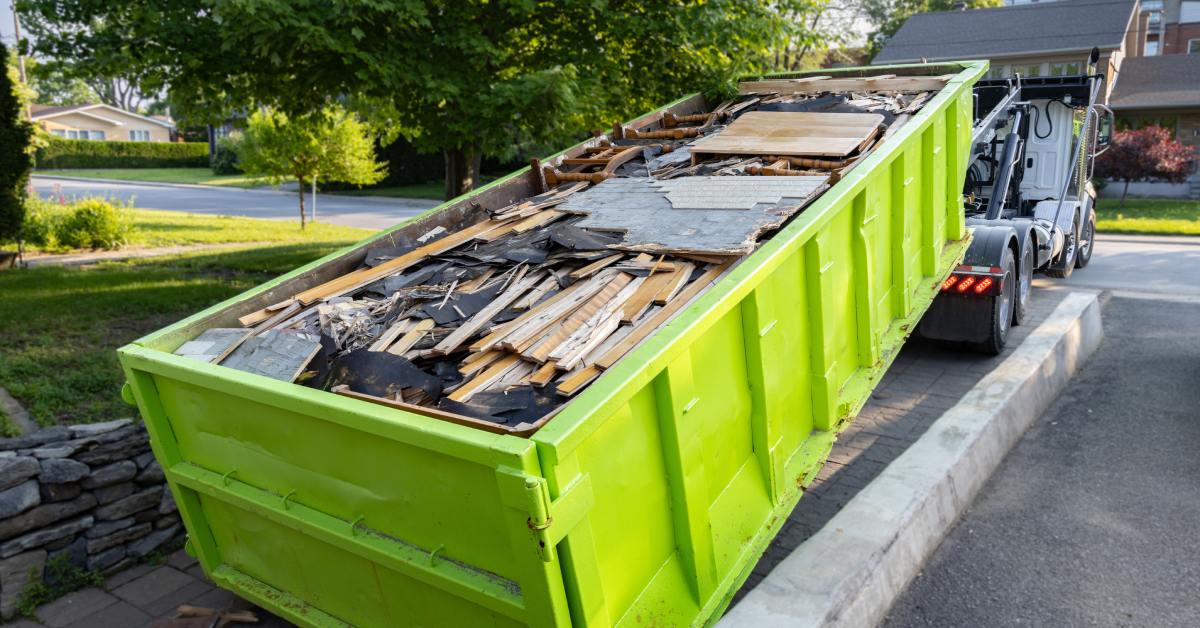 A lime green dumpster full of debris from a home renovation is loaded onto a truck in a home driveway.